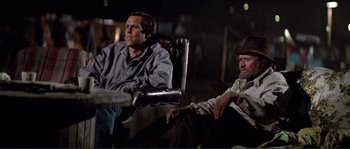 Movie still from “They Live” (1988), directed by John Carpenter – Two men sitting in a chair in a dark room; Medium shot, Low angle