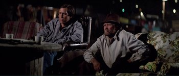 Movie still from “They Live” (1988), directed by John Carpenter – Two men sitting next to each other on a chair; Wide shot, Low angle