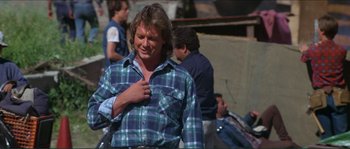 Movie still from “They Live” (1988), directed by John Carpenter – A man in a plaid shirt is standing in front of a group of people; Medium shot, Low angle