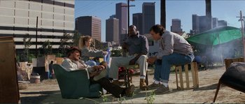 Movie still from “They Live” (1988), directed by John Carpenter – A group of people sitting on the side of a road; Wide shot, High angle