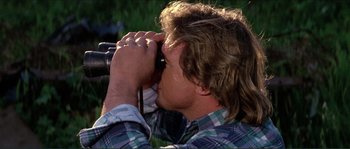 Movie still from “They Live” (1988), directed by John Carpenter – A man looking through binoculars while wearing a plaid shirt; Close Up shot, Over the shoulder angle