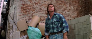 Movie still from “They Live” (1988), directed by John Carpenter – A man standing next to a pile of cardboard; Medium shot, Low angle