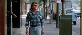 Movie still from “They Live” (1988), directed by John Carpenter – A man walking down the street holding a cell phone; Medium shot, Low angle