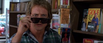Movie still from “They Live” (1988), directed by John Carpenter – A man wearing sunglasses and a plaid shirt in a store; Close Up shot, Low angle