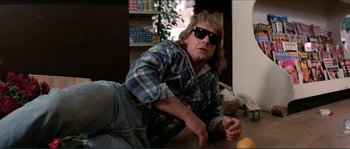 Movie still from “They Live” (1988), directed by John Carpenter – A man in a plaid shirt is laying on the ground; Medium shot, Low angle