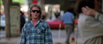 Movie still from “They Live” (1988), directed by John Carpenter – A man in plaid shirt and sunglasses on a street; Medium shot, Low angle
