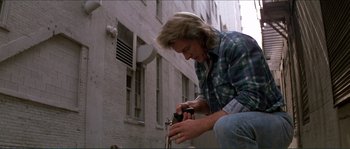 Movie still from “They Live” (1988), directed by John Carpenter – A man in a plaid shirt is holding a camera; Medium shot, Low angle