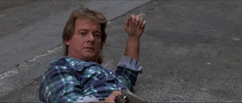 Movie still from “They Live” (1988), directed by John Carpenter – A man laying on the ground holding a gun in his hand; Medium shot, High angle