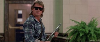 Movie still from “They Live” (1988), directed by John Carpenter – A man in a plaid shirt holding a laptop; Medium shot, Low angle
