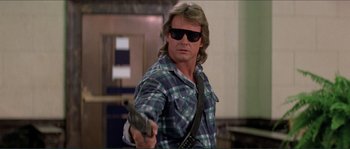 Movie still from “They Live” (1988), directed by John Carpenter – A man holding a gun while wearing sunglasses and a plaid shirt; Medium shot, Low angle
