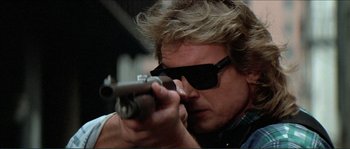 Movie still from “They Live” (1988), directed by John Carpenter – A man wearing sunglasses is holding a gun; Close Up shot, Low angle