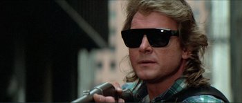 Movie still from “They Live” (1988), directed by John Carpenter – A person wearing sunglasses holding a microphone; Close Up shot, Low angle
