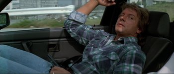 Movie still from “They Live” (1988), directed by John Carpenter – A man sitting in the driver's seat of a car; Medium shot, Low angle