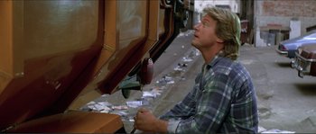 Movie still from “They Live” (1988), directed by John Carpenter – A man in a plaid shirt looking into a dumpster; Medium shot, Low angle