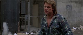 Movie still from “They Live” (1988), directed by John Carpenter – A man in plaid shirt standing in front of a fence; Medium shot, Low angle