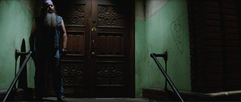 Movie still from “They Live” (1988), directed by John Carpenter – A door way with a wooden handle and a green wall; Wide shot, High angle
