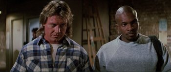 Movie still from “They Live” (1988), directed by John Carpenter – A man standing next to another man in front of a ladder; Medium shot, Low angle