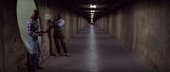 Movie still from “They Live” (1988), directed by John Carpenter – A man holding a baseball bat while standing in a hallway; Wide shot, High angle