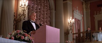 Movie still from “They Live” (1988), directed by John Carpenter – A man in a tuxedo standing at a podium; Medium shot, Low angle