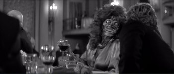 Movie still from “They Live” (1988), directed by John Carpenter – A woman with a creepy face sitting at a table with a glass of red wine; Close Up shot, Over the shoulder angle