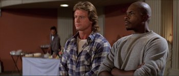 Movie still from “They Live” (1988), directed by John Carpenter – A man in a plaid shirt is standing next to another man in a gray shirt; Medium shot, Low angle