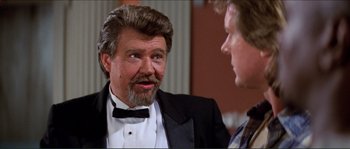 Movie still from “They Live” (1988), directed by John Carpenter – A man in a tuxedo talking to another man in a suit; Close Up shot, Over the shoulder angle