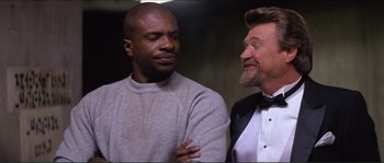 Movie still from “They Live” (1988), directed by John Carpenter – A man and a man standing next to each other; Medium shot, Low angle