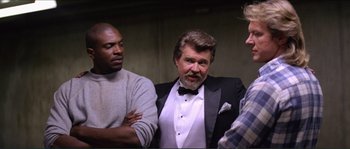 Movie still from “They Live” (1988), directed by John Carpenter – A group of men standing next to each other in a room; Medium shot, Low angle