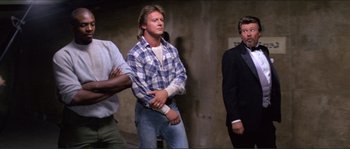Movie still from “They Live” (1988), directed by John Carpenter – A group of men standing next to each other in a room; Medium shot, Low angle