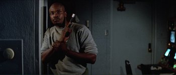 Movie still from “They Live” (1988), directed by John Carpenter – A man holding a hammer in a room; Medium shot, Low angle