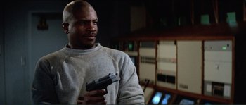 Movie still from “They Live” (1988), directed by John Carpenter – A man holding a gun while standing in a room; Close Up shot, Low angle