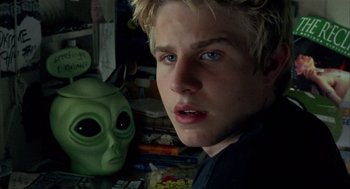 Movie still from “Thirteen” (2003), directed by Catherine Hardwicke – A young man standing next to a green alien mask; Close Up shot, Over the shoulder angle