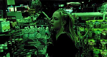 Movie still from “Thirteen” (2003), directed by Catherine Hardwicke – A woman standing next to a store filled with lots of bottles; Medium shot, High angle