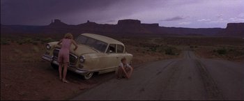 Movie still from “This Boy's Life” (1993), directed by Michael Caton-Jones – A man kneeling down next to an old car on the side of the road; Wide shot, High angle