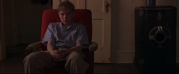 Movie still from “This Boy's Life” (1993), directed by Michael Caton-Jones – A young man sitting in a chair in front of a door; Medium shot, High angle
