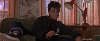 Movie still from “This Boy's Life” (1993), directed by Michael Caton-Jones – A man sitting on top of a couch holding a cell phone; Medium shot, Low angle