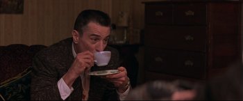 Movie still from “This Boy's Life” (1993), directed by Michael Caton-Jones – A man is drinking a cup of coffee from a saucer; Medium shot, High angle