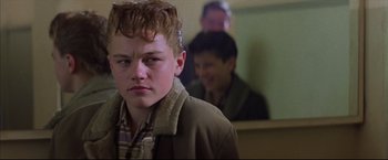 Movie still from “This Boy's Life” (1993), directed by Michael Caton-Jones – A young man in a brown jacket in front of two other men; Close Up shot, Low angle