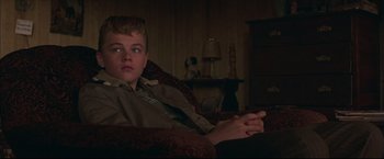 Movie still from “This Boy's Life” (1993), directed by Michael Caton-Jones – A boy sitting on a couch in a living room; Medium shot, High angle