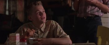 Movie still from “This Boy's Life” (1993), directed by Michael Caton-Jones – A young man sitting at a table in a room; Medium shot, Low angle