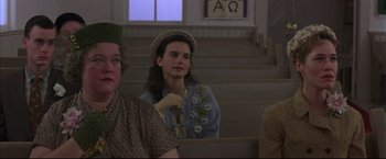 Movie still from “This Boy's Life” (1993), directed by Michael Caton-Jones – A woman sitting on a bench in front of other people; Medium shot, Over the shoulder angle