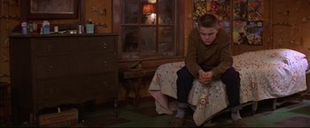 Movie still from “This Boy's Life” (1993), directed by Michael Caton-Jones – A young boy sitting on a bed in front of a window; Medium shot, High angle