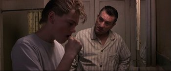Movie still from “This Boy's Life” (1993), directed by Michael Caton-Jones – A man standing next to a young man in a room; Medium shot, Low angle