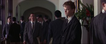 Movie still from “This Boy's Life” (1993), directed by Michael Caton-Jones – A young man in a suit and tie standing in front of a group of men; Medium shot, Low angle
