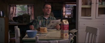 Movie still from “This Boy's Life” (1993), directed by Michael Caton-Jones – A man sitting at a dinner table reading a newspaper; Medium shot, Low angle