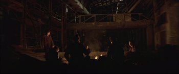 Movie still from “This Boy's Life” (1993), directed by Michael Caton-Jones – A group of people standing in front of an open fire pit; Wide shot, Low angle