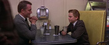 Movie still from “This Boy's Life” (1993), directed by Michael Caton-Jones – Two people sitting at a table with drinks; Medium shot, Over the shoulder angle