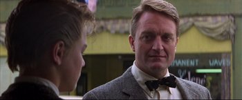 Movie still from “This Boy's Life” (1993), directed by Michael Caton-Jones – A man wearing a suit and bow tie talking to another man; Close Up shot, Low angle