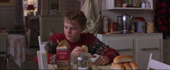 Movie still from “This Boy's Life” (1993), directed by Michael Caton-Jones – A young boy sitting at a table eating a sandwich; Medium shot, Over the shoulder angle