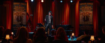 Movie still from “This Is 40” (2012), directed by Judd Apatow – A man standing in front of a microphone in front of a crowd; Wide shot, Over the shoulder angle
